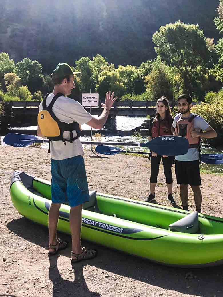 Two adults listening to an instructor explain river rafting and kayaking safety during a training class on the Provo River Utah.