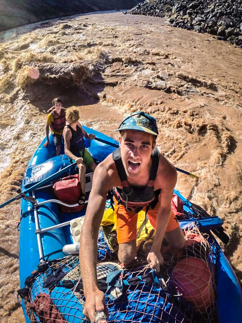 Three guys in a selfie photo who are rafting through a whitewater rapid on the Colorado River in the Grand Canyon.