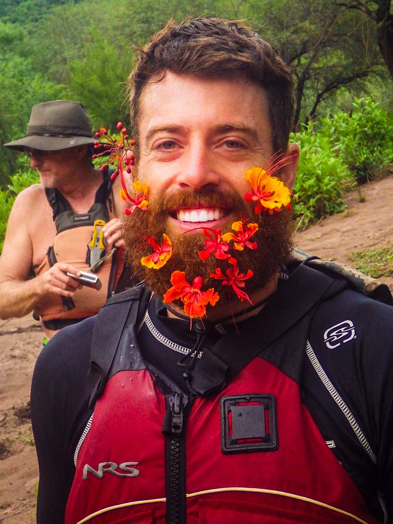 A man wearing wild flowers in hs beard during a whitewater river rafting trip in Mexico.