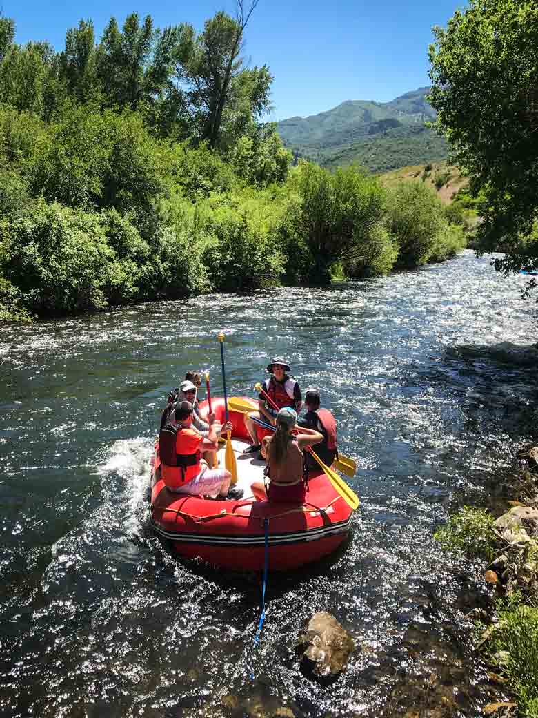 A group of people rafting in a red raft on the Provo River near Orem and Park City Utah.