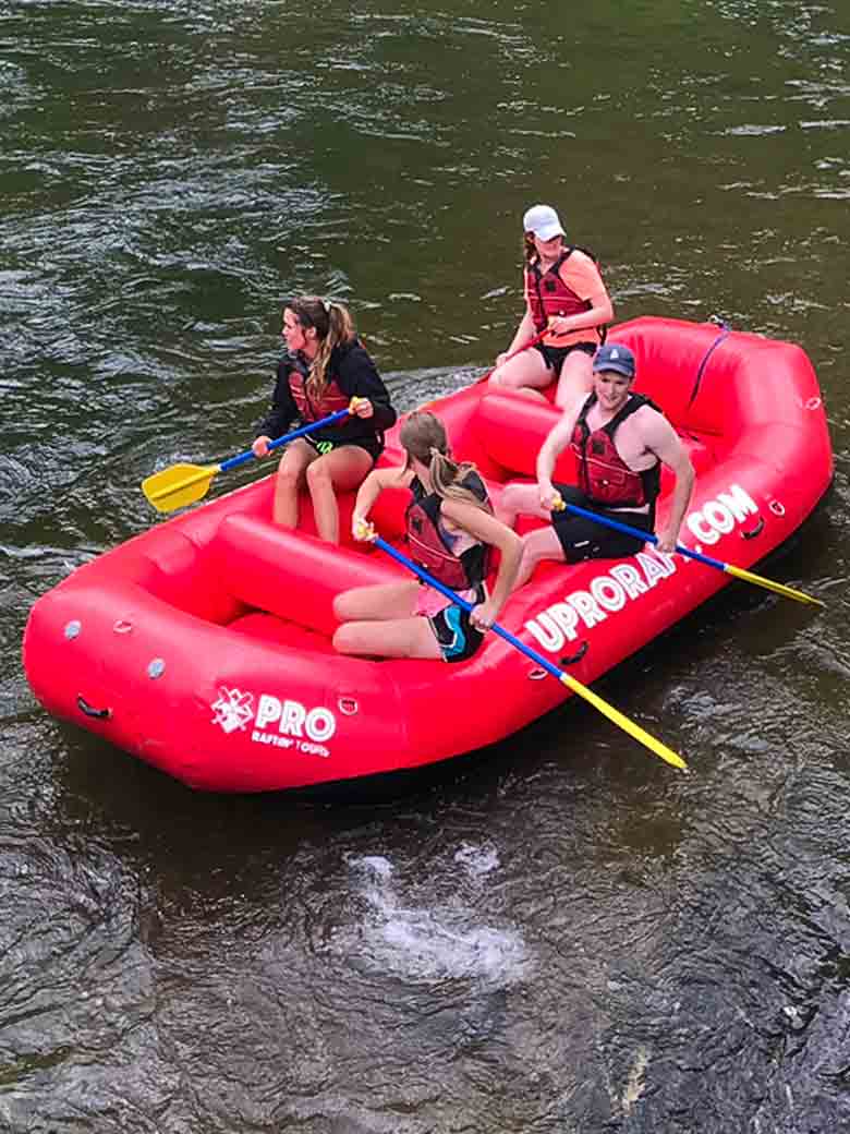 A group of three rafting in a red raft on the Provo River near Provo and Park City Utah.