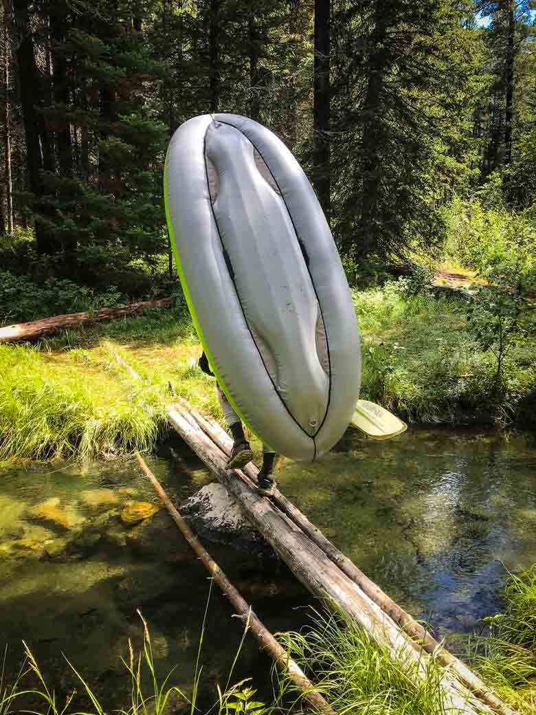 Man carrying an inflatable kayak across a log during a whitewater rafting trip.