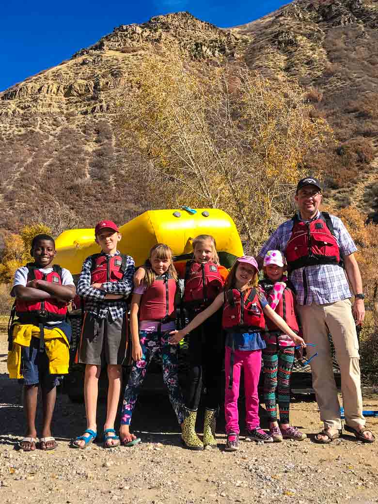 A man with six children standing in front of a yellow raft before they take a youth river skills training class on the Provo River in Utah.